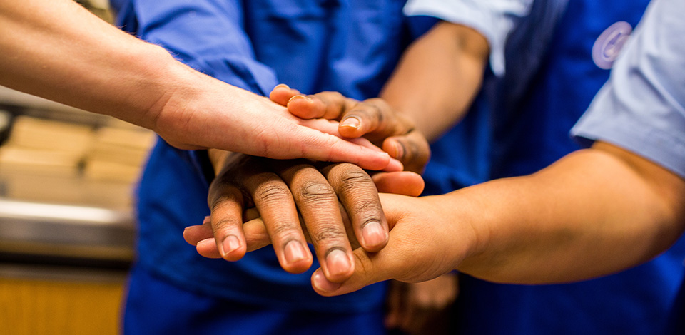 Team in restaurant in huddle, hands one on top of another